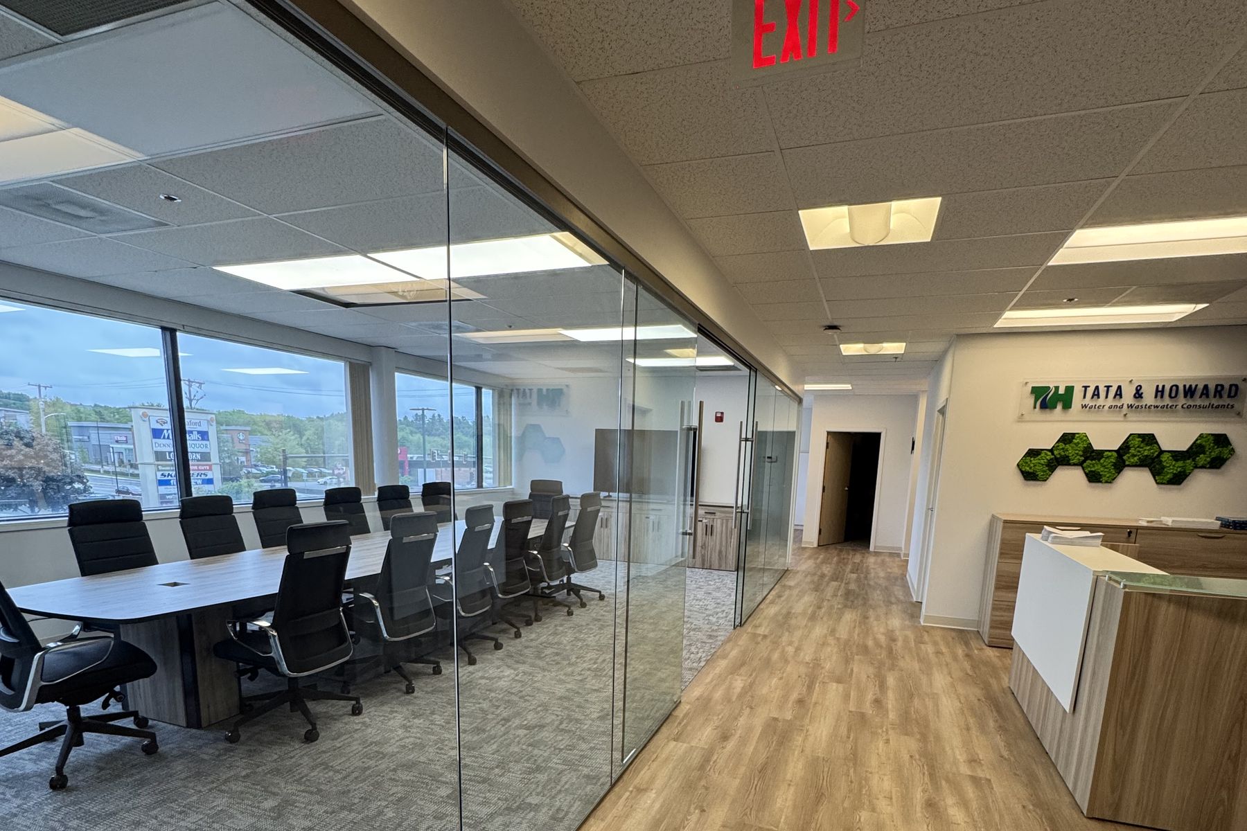 The same Tata & Howard entrance after install, with a finished plank floor, glass-enclosed conference room, and the reception desk at the end of the corridor