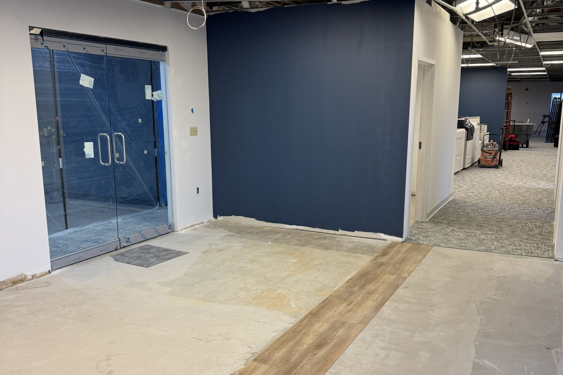 Tata & Howard suite entrance before install, with bare concrete floor, a painted navy accent wall, and the plank floor one run in