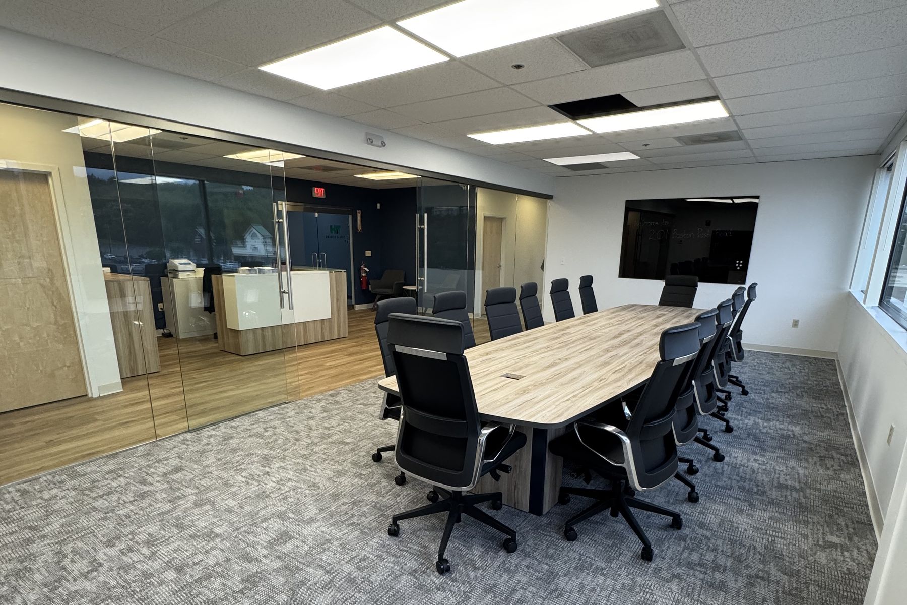 The finished glass-enclosed conference room at Tata & Howard, with a woodgrain table, black executive seating, and a wall-mounted display