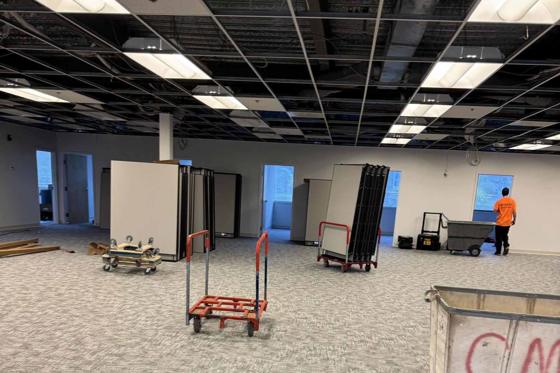 Open floor plate at Tata & Howard before install, with systems furniture panels staged on carts and the ceiling grid open