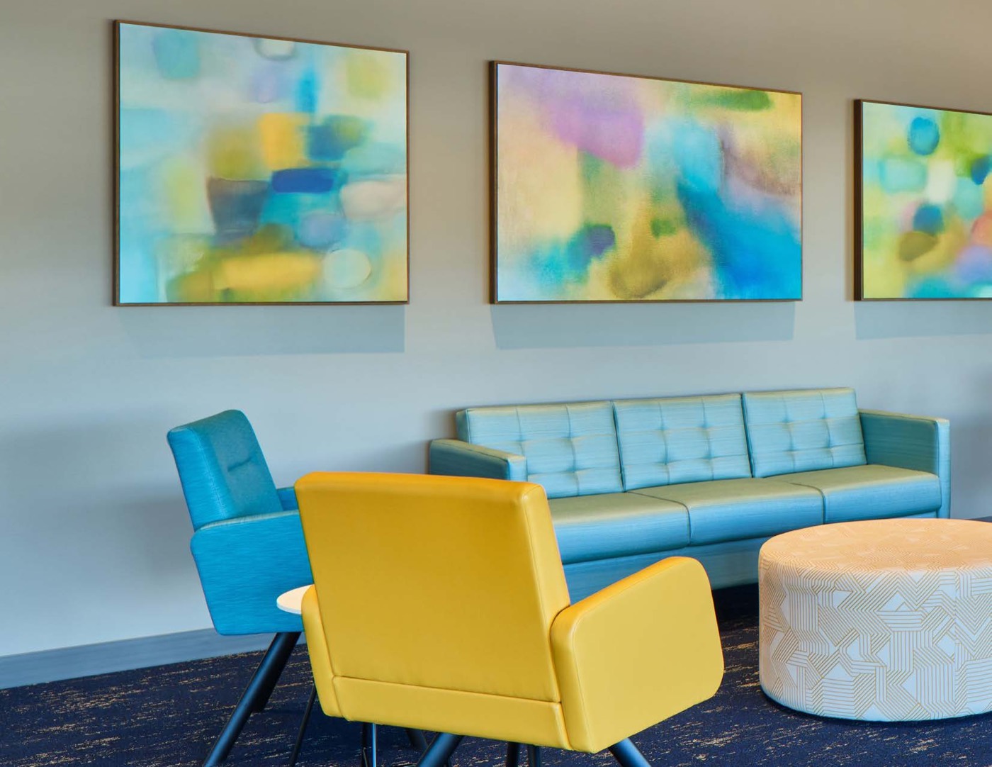 Three framed abstract paintings hung above blue and yellow lounge seating in a healthcare waiting area