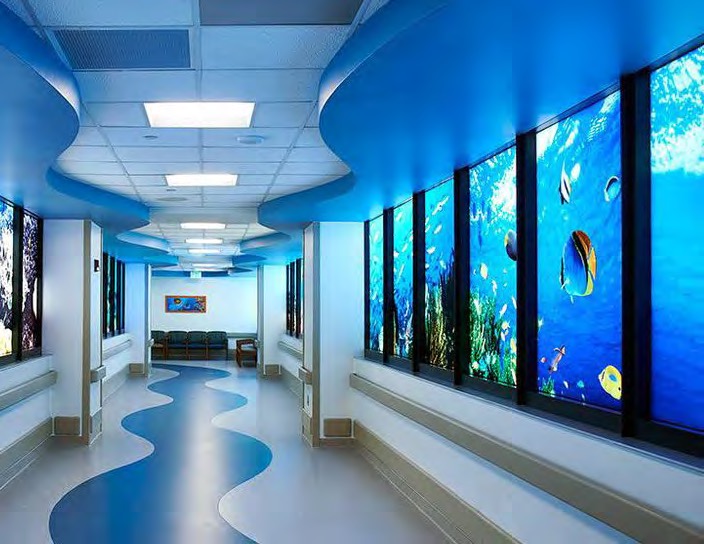 Hospital corridor lined with backlit underwater reef films, giving the wall an aquarium appearance