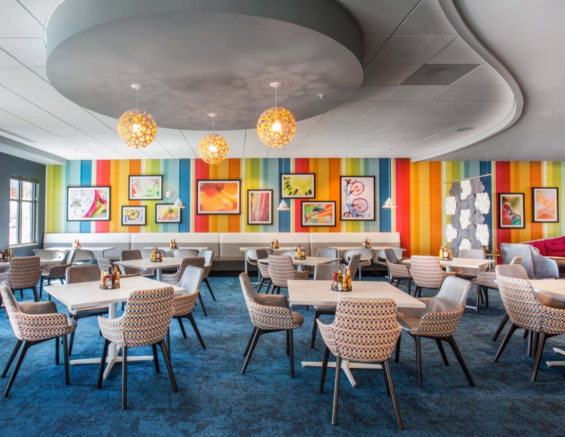 Framed artwork on a striped multicolour wall above banquette seating in a senior living dining room